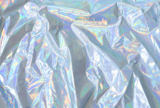 Closeup View Of Crumpled Holographic Fabric With Soft Metallic Sheen And Shifting Pastel Rainbow Reflections, Forming Abstract Folds And Luminous Texture For Festive Backgrounds