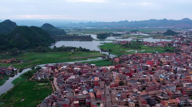 Aerial panorama of a waterside settlement surrounded by karst mountains and green fields, with water networks and residential buildings.
