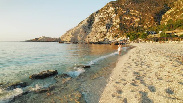Young woman strolls along beach at sunset in Kefalonia on a warm summer evening