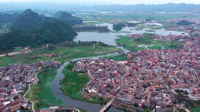 This is an aerial landscape showing a lakeside town surrounded by karst mountains, with waterways and grasslands nearby.