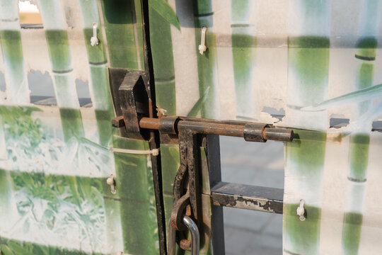 an old rusty slide bolt on a torn plastic bamboo gate.