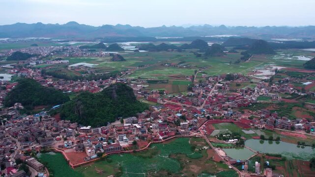 This is an aerial landscape showing a rural settlement surrounded by karst hills, wetlands and farmland under a hazy sky.