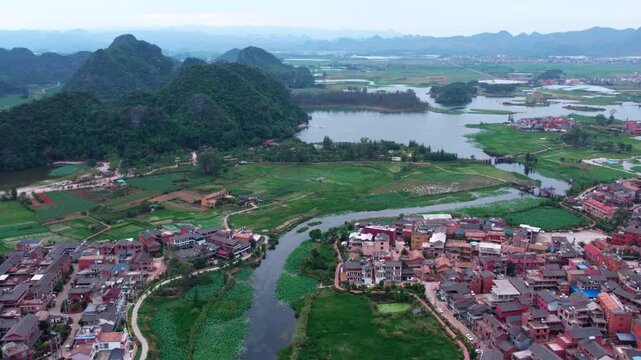 An aerial shot shows a rural village beside a river, surrounded by karst mountains and wetlands.