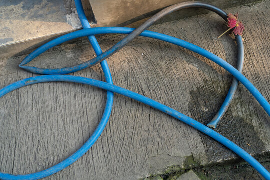 Tangled blue plastic garden hose with a damaged blackened section on rough concrete.