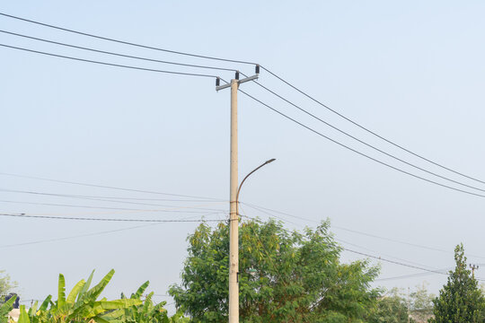 Concrete utility pole with overhead power lines and street lamp against clear sky.