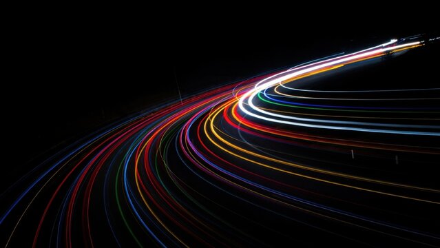 Long exposure night traffic light trails on highway curve creating colorful motion blur effect.