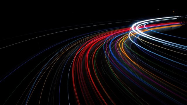 Vibrant neon light streaks from night traffic on highway curve for urban transport concept.