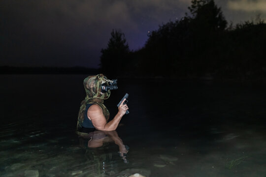 Armed combat diver with night vision holding pistol during night covert mission