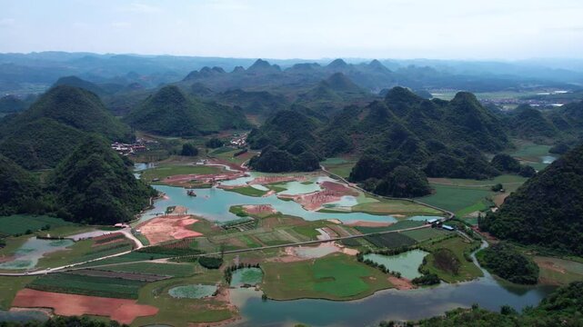 A panoramic view of a karst landscape with scattered lakes, agricultural fields, and forested hills under a clear sky.