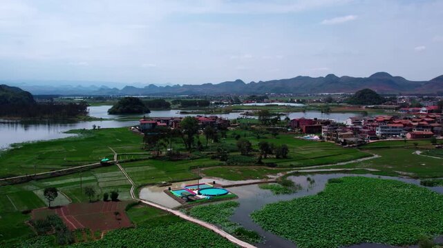A rural settlement situated among lakes, fields and karst mountains, with lush greenery and calm waters.