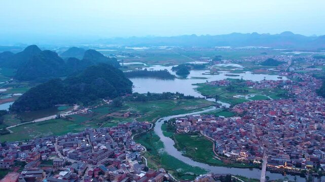 An aerial panoramic landscape featuring karst peaks, a winding river, and a clustered water settlement in a rural area.