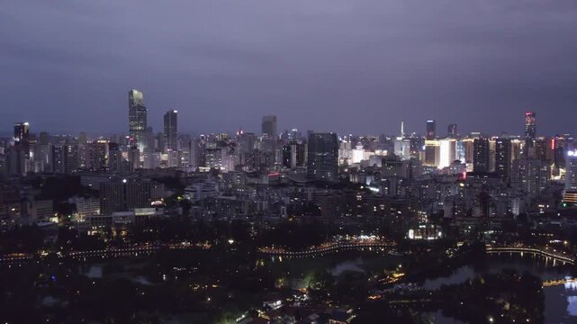 A high-angle panoramic view of an illuminated urban cityscape at night, featuring dense buildings and a waterfront area.
