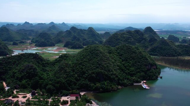 Aerial view of karst mountains covered with dense forest, a calm lake and surrounding natural valleys on a clear day.