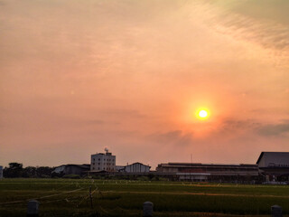 Fototapeta premium Sun sets softly over rural fields and low buildings