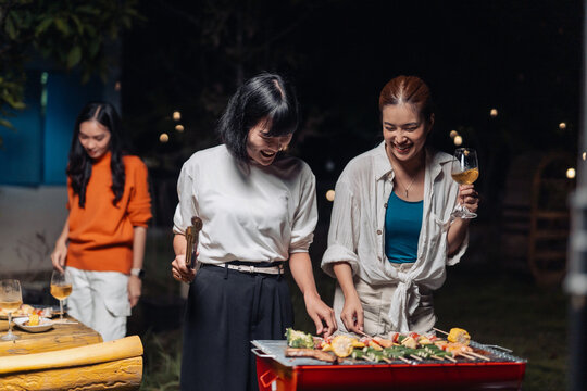 Friends grilling bbq food and drinking wine at night