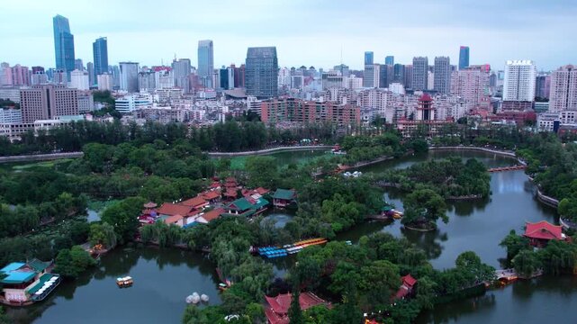 A panoramic view of an urban park with lakes, traditional architecture, and a modern city skyline in the background.