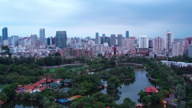 A high-angle view of a modern city skyline with a large central park featuring lakes and trees, plus traditional buildings.