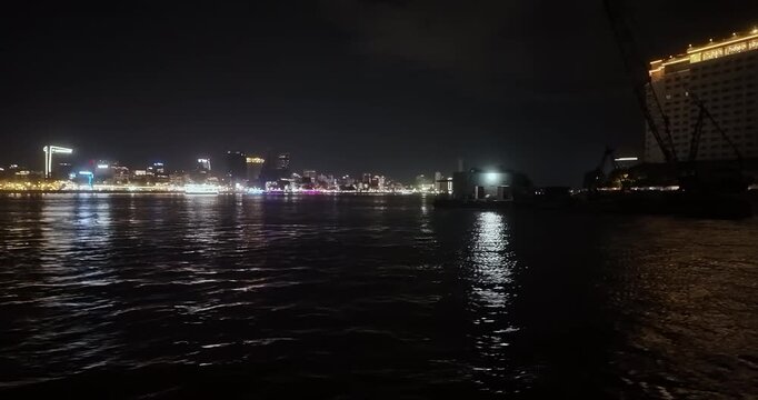 Night view from a ferry passing by a construction crane on a barge on the Mekong River, with the Phnom Penh skyline in the background.