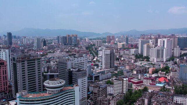 Panoramic daytime aerial view of a dense urban area with mixed buildings, backed by distant mountains under a clear sky.