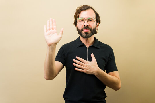 Hispanic man making an oath with hand on chest and raised hand showing loyalty, sincerity, promise, and integrity