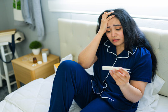 Woman feeling worried and overwhelmed after getting an unexpected positive pregnancy test result in her bedroom