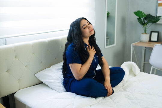 Latin woman meditating in bed, practicing mindfulness and deep breathing for stress relief and self-care at home