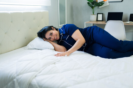 Young woman relaxing on a soft bed in her bedroom, feeling well-rested and happy in comfortable sleepwear
