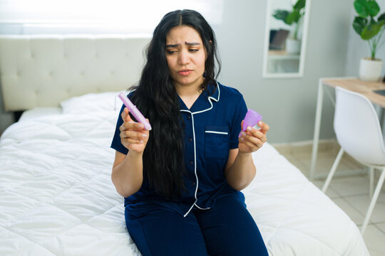 Young woman choosing between tampon and menstrual cup for period protection, thinking about feminine hygiene products