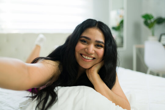 Selfie of a woman in bed, smiling and relaxing in her bedroom enjoying morning comfort