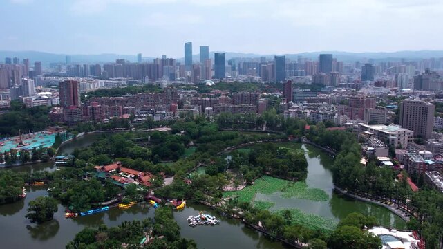 A high-angle shot showing a city park with lakes and boats, backed by a modern urban skyline.