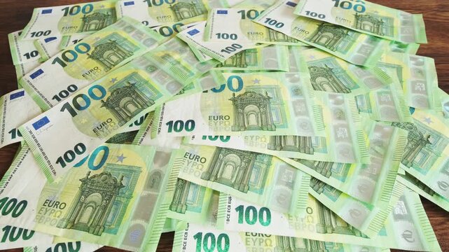 Pile of one hundred euro banknotes on wooden table. Cash background representing wealth, success and financial profit, 4k