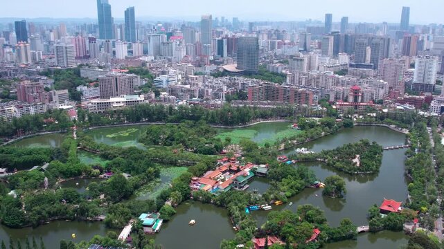 Aerial view of an urban park with lakes, surrounded by city high-rise buildings and dense greenery.