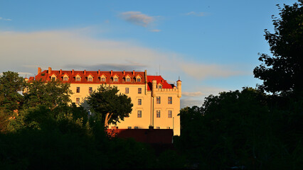 Historic Castle With Red Roof Bathed in Golden Sunset Light Behind Summer Trees - Ryn Castle in Masuria. © Pol Badger