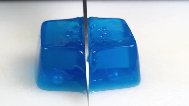 Transparent Blue Jelly Cube Slowly Sliced with Sharp Kitchen Knife in Macro View