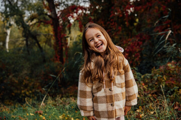 Naklejka premium Joyful child enjoying autumn in a plaid coat amidst colorful foliage.