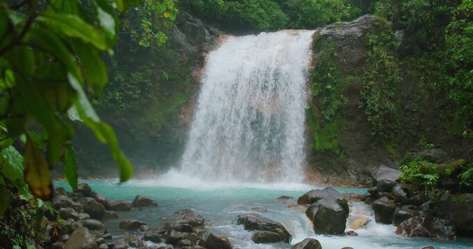 Waterfall crashing over cliff into turquoise pool and stream during rainy weather in rainforest of Costa Rica