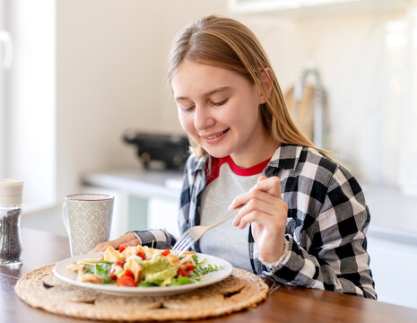 Smiling girl enjoys fresh vegetable meal on wooden table at home during the bright daytime