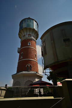 A historic red brick water tower converted into an observation tower against a clear blue sky with an outdoor caf&eacute; patio below - the Masurian town of Pisz.