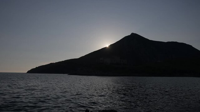 Sun setting over the silhouette of a high hill above the sea. Beautiful sunset over the ocean with mountain silhouettes.