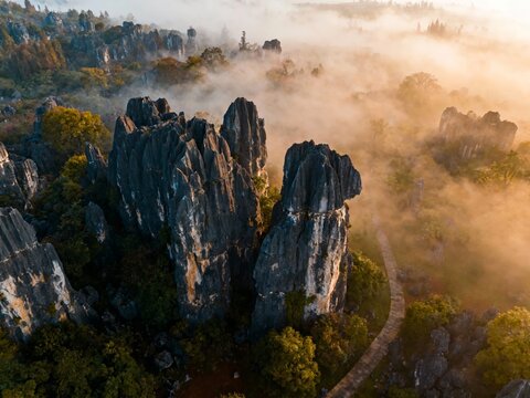 Aerial view of mist-covered limestone karsts at sunrise with winding path through forested landscape