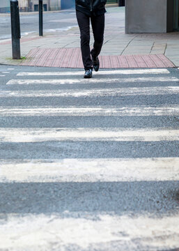 A person dressed in black walks across a pedestrian crosswalk in an urban area, likely commuting to their destination.
