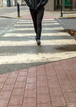 A person wearing a black leather jacket and trousers walks across a city zebra crossing, navigating the urban street to reach their destination.