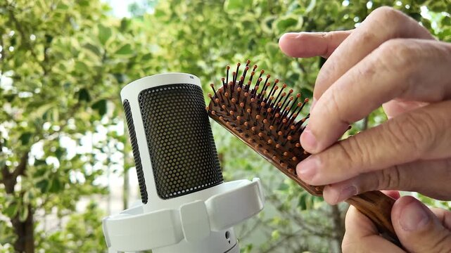 Close up hand tapping wooden hairbrush bristles near condenser microphone for ASMR sound triggers concept