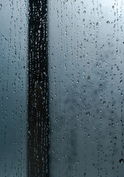 Raindrops on a glass window pane during a cloudy day