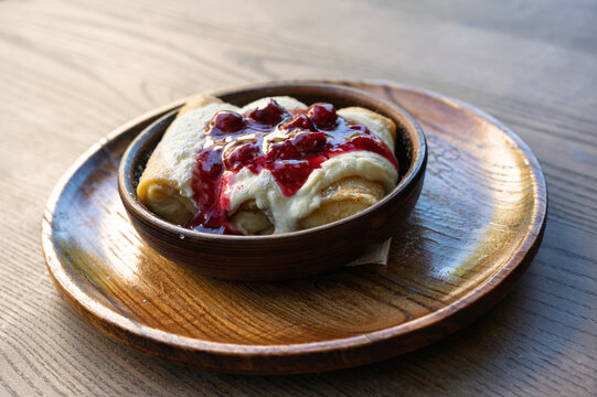 Delicious crepes with cream and berry sauce on a wooden plate