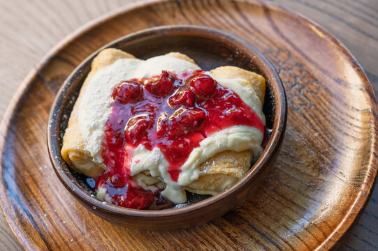 Delicious crepes with sweet cream and cherry jam served in a rustic wooden bowl