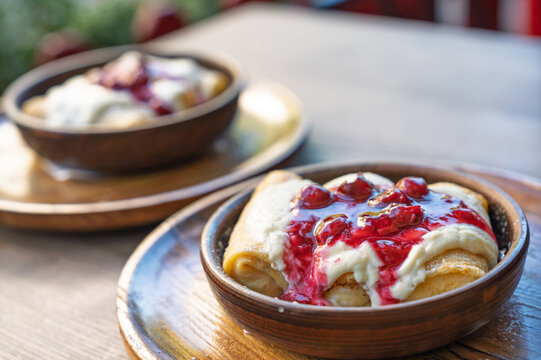 Two bowls of delicious crepes with sweet cream and berry jam on a wooden table