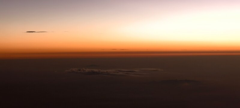 Serene aerial view of sunrise or sunset with a soft gradient from light purple to warm orange. Layers of mist and clouds create depth, while darker formations add contrast. 