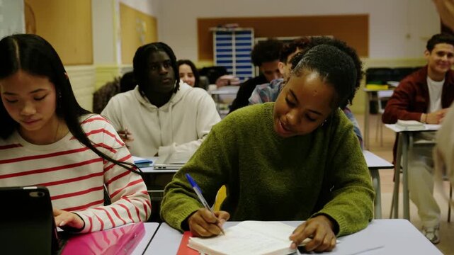 Multiethnic teenage students sitting at desks in a classroom paying attention during a lesson
