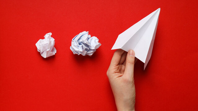 Hand Throwing White Paper Airplane with Crumpled Paper on Red
